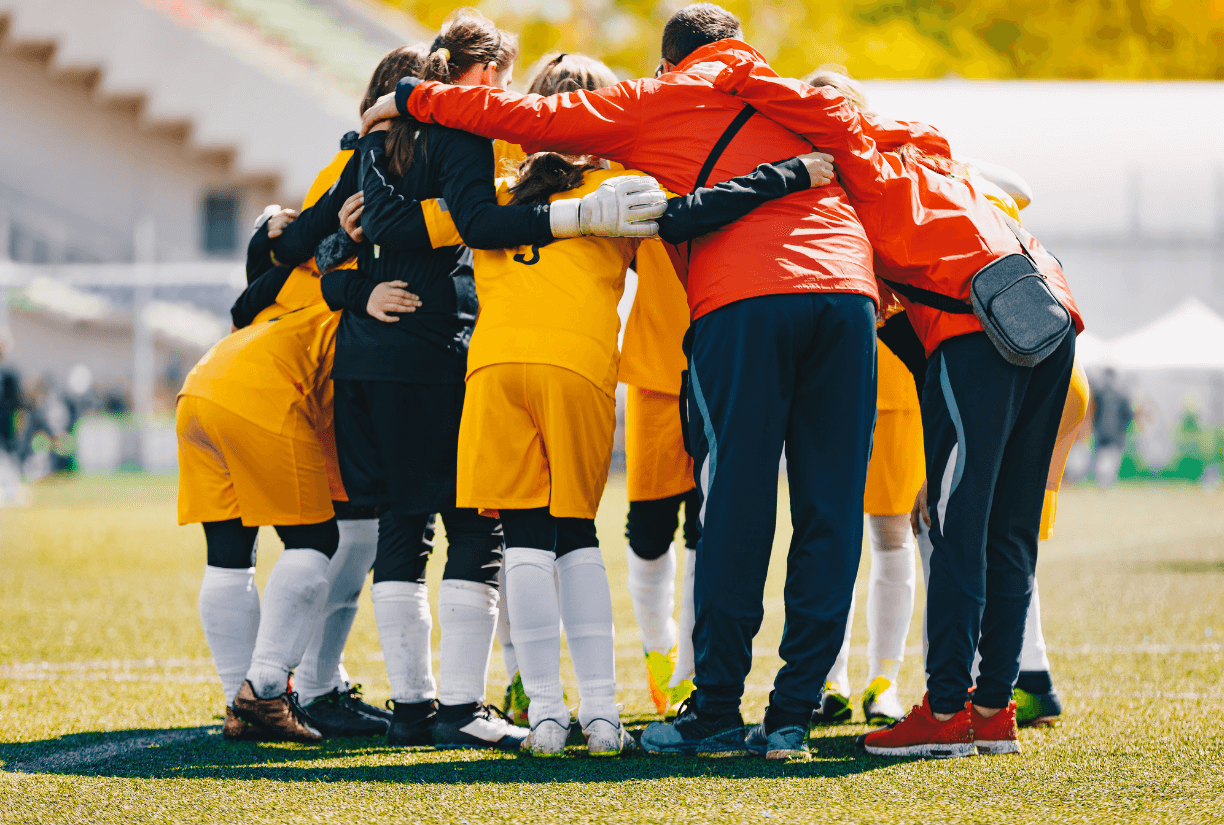 Coach And Team Huddle On Soccer Pitch